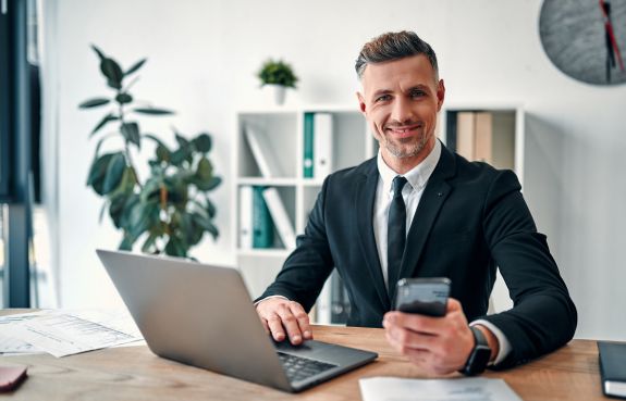 A successful businessman in a modern office, working with a laptop and smartphone, illustrating how to become a business tycoon.